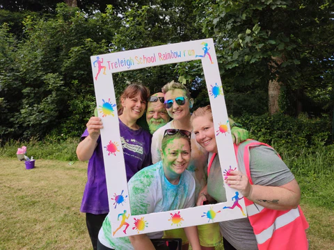 Group of people holding a colorful photo frame outdoors with trees in the background.
